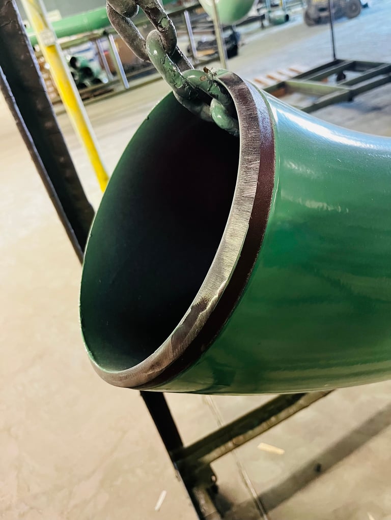 Close-up of a green industrial pipe with metal band clamp, displayed in a warehouse or factory setting